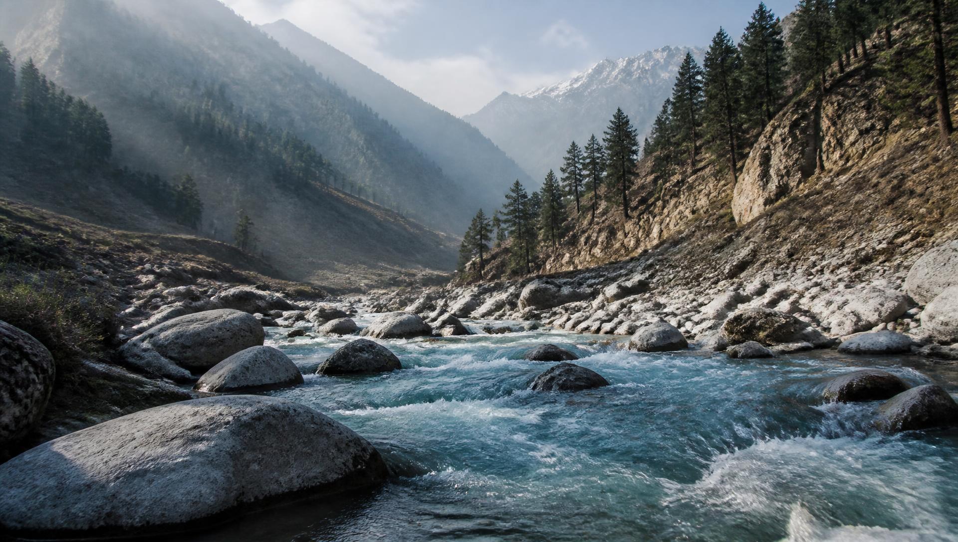 Fast, clear Himalayan river between boulders under misty forested ridges